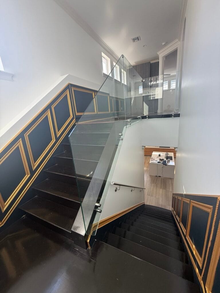 Frameless glass stair railing with stainless standoffs on a black staircase in Boca Raton
